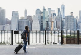 Woman with suitcase in Brooklyn looking over the East River at Manhattan