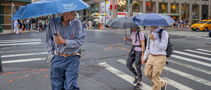 People with umbrellas crossing 5th Avenue