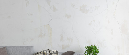 An apartment wall with cracks above a sofa.
