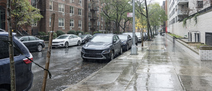 Drenched cars parked in a rain downpour in uptown New York City. Apartment buildings and brownstone row houses line this upper east side Manhattan residential district one way street and sidewalk scene.