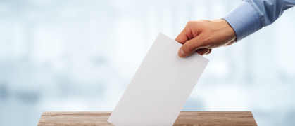 A disembodied hand puts a ballot in a voting box.