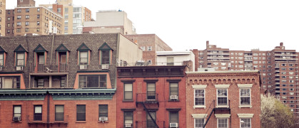 Three brownstone buildings in Manhattan backed by larger apartment complexes.