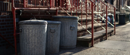 A row of old metal garbage cans outside an urban neighborhood home along a sidewalk in Astoria Queens New York