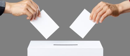 Two hands about to drop ballots into a voting box on a grey background.