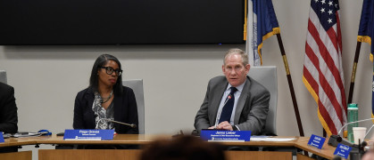 An older man at a desk in the MTA offices near a younger woman.