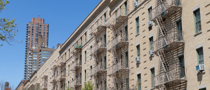 A row of similar old brick residential buildings with fire escapes on the Upper East Side of New York City