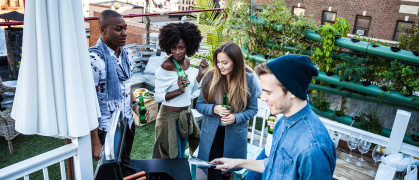 Friends having fun, grilling BBQ and drinking beers together during a rooftop party in New York East Village.