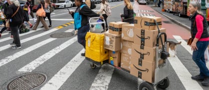 A driver pulls a trolley with Amazon Prime packages across a NYC street.