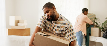 Man carrying a moving box in the middle of a move-prepped living room