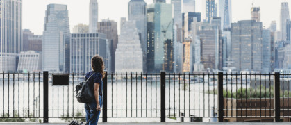 Woman with suitcase in Brooklyn looking over the East River at Manhattan